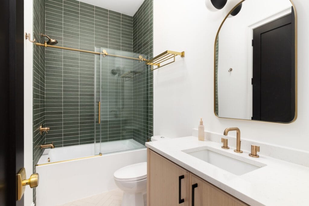 A bathroom with gold accents and a shower with green subway tiles. bathroom-tile-repair-tile-installation-good-morning-contracting
